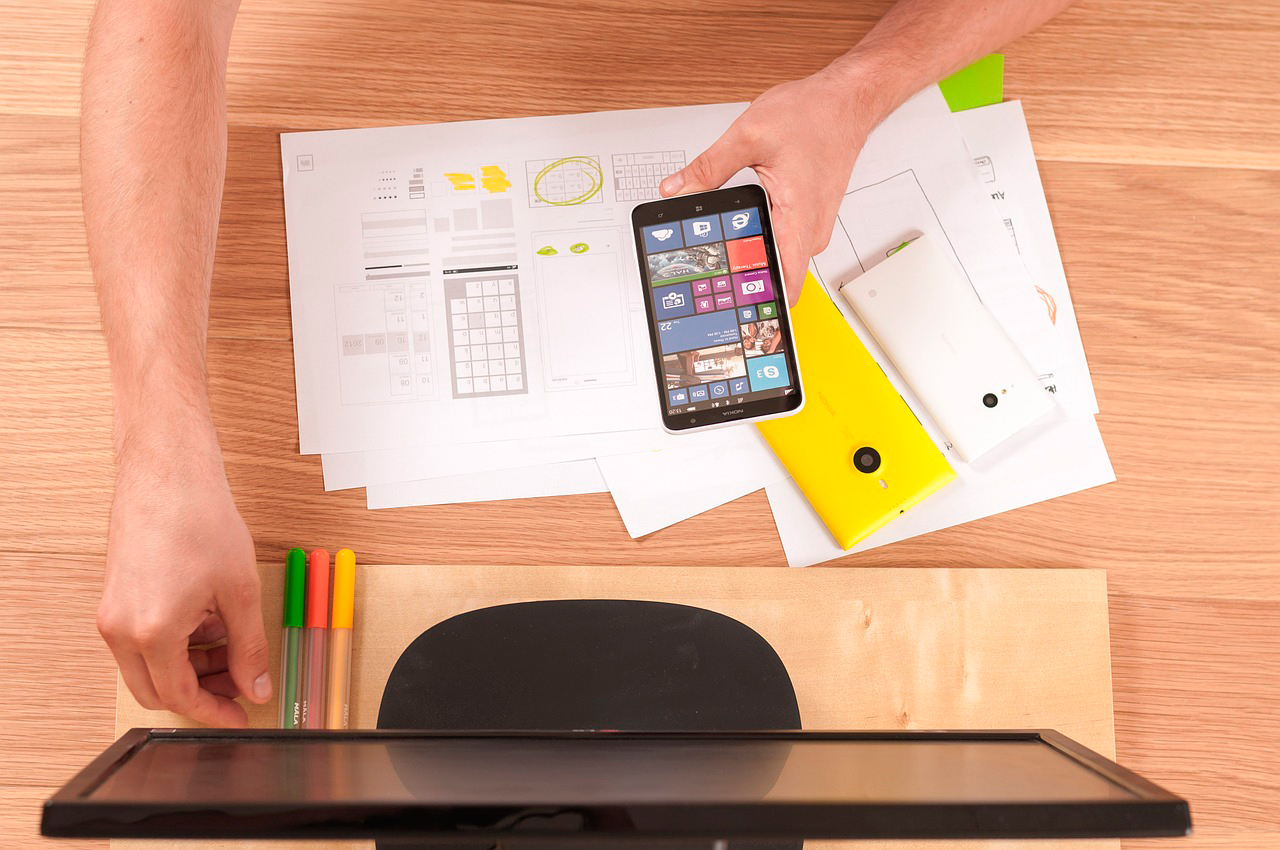 Working table of an app developer with a mobile, computer and some papers